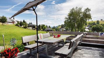 An outdoor seating area with picnic tables and benches, a metal umbrella, and a flower arrangement.