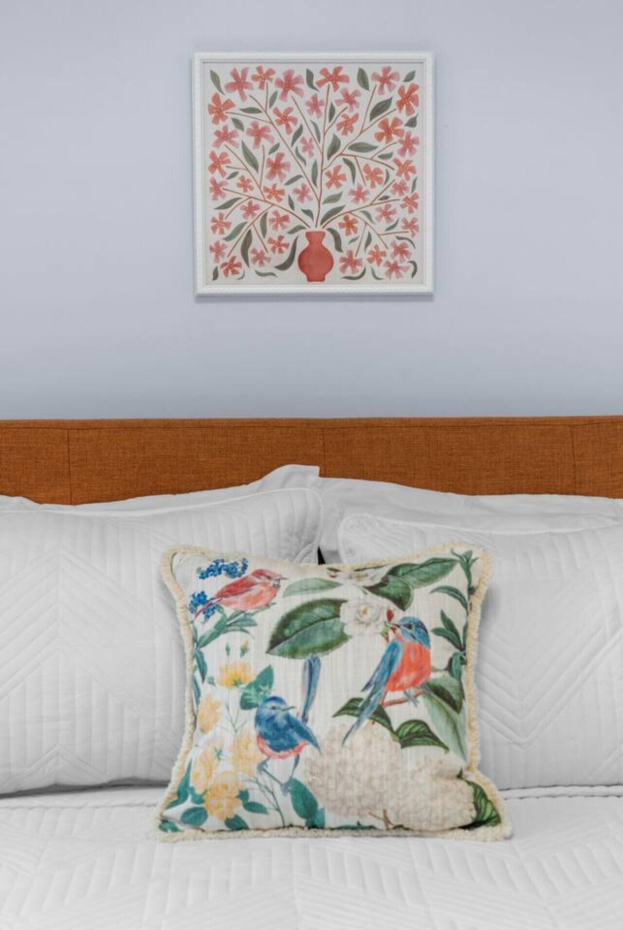 Una cama con ropa blanca y un cojín decorativo con pájaros y flores.