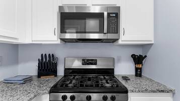 Una cucina con mobili bianchi, un forno a microonde in acciaio inox, un fornello a gas e set di coltelli sul piano di lavoro.