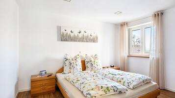 A bedroom with a wooden bed, a nightstand, a wall-mounted artwork, and a window with curtains.