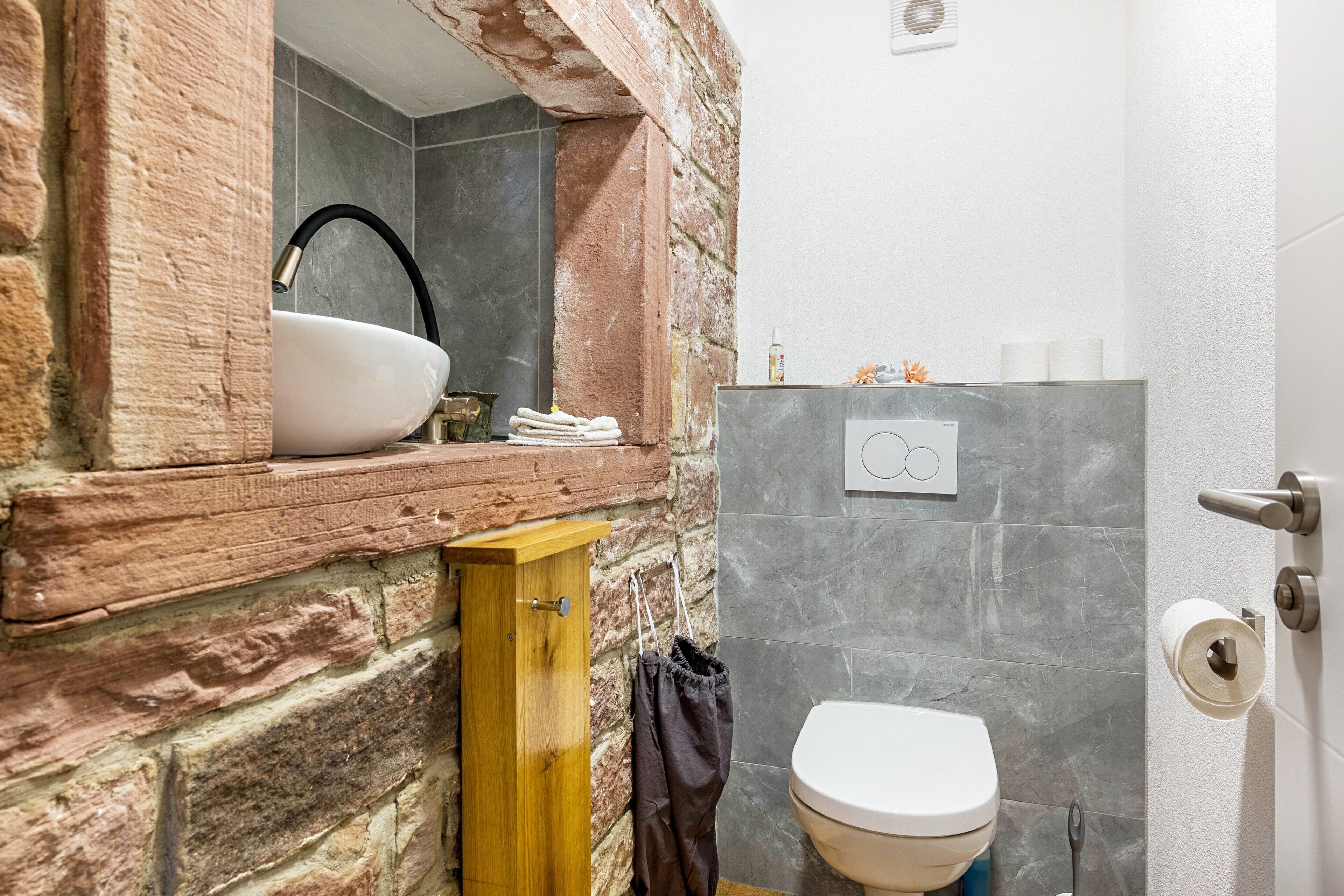 A bathroom with a stone wall, a wooden cabinet, a sink, and a toilet.