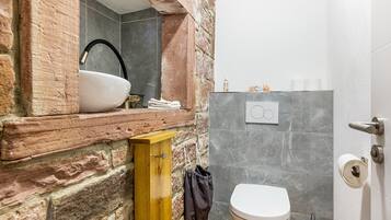 A bathroom with a stone wall, a wooden cabinet, a sink, and a toilet.