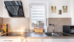 A modern kitchen with a built-in oven, a microwave, a sink, and a window with blinds. - Apartment 'Seyfried' with Private Terrace, Shared Garden and Wi-Fi (Hardheim)