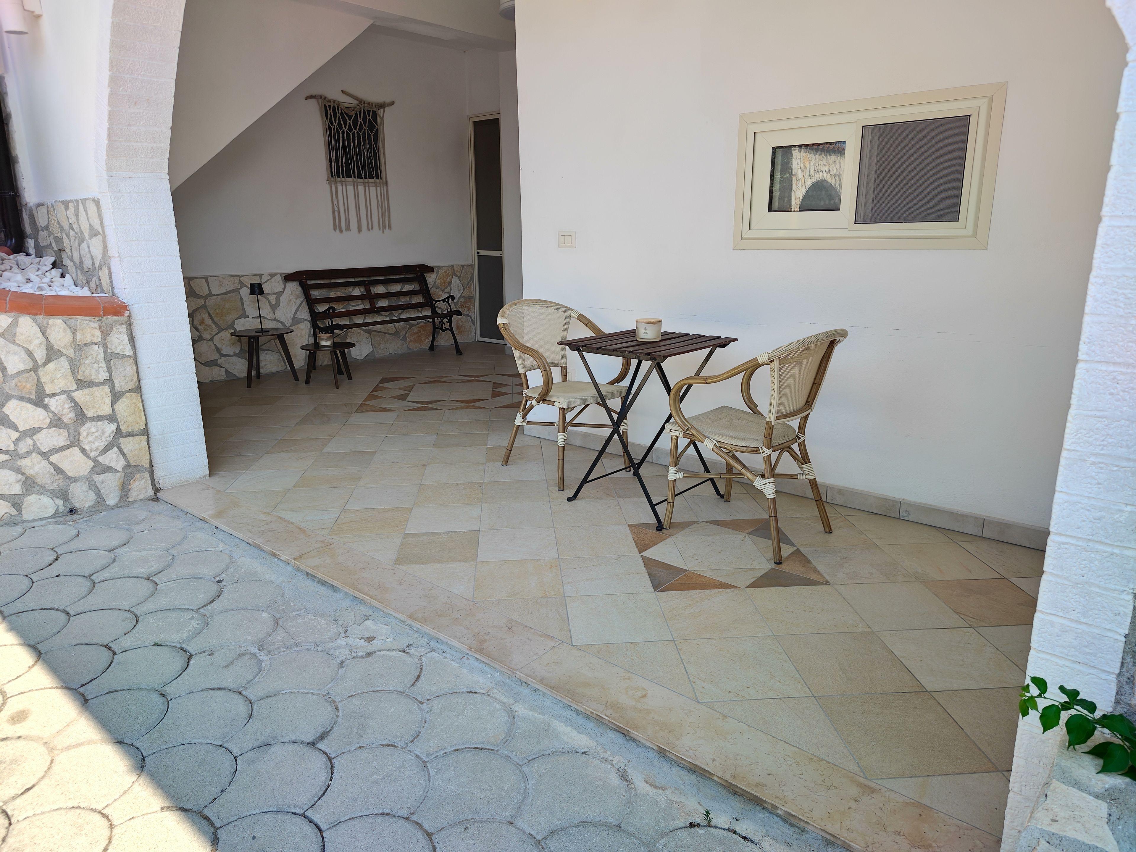 Un área de estar al aire libre con una mesa y sillas, un muro de piedra y una escalera que lleva a un nivel superior.