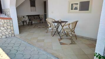 Un área de estar al aire libre con una mesa y sillas, un muro de piedra y una escalera que lleva a un nivel superior.