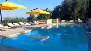 A swimming pool with lounge chairs and yellow umbrellas, surrounded by a stone wall and trees.