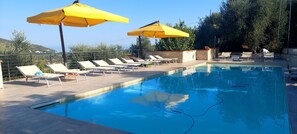 A swimming pool with lounge chairs and yellow umbrellas, surrounded by a stone wall and trees.