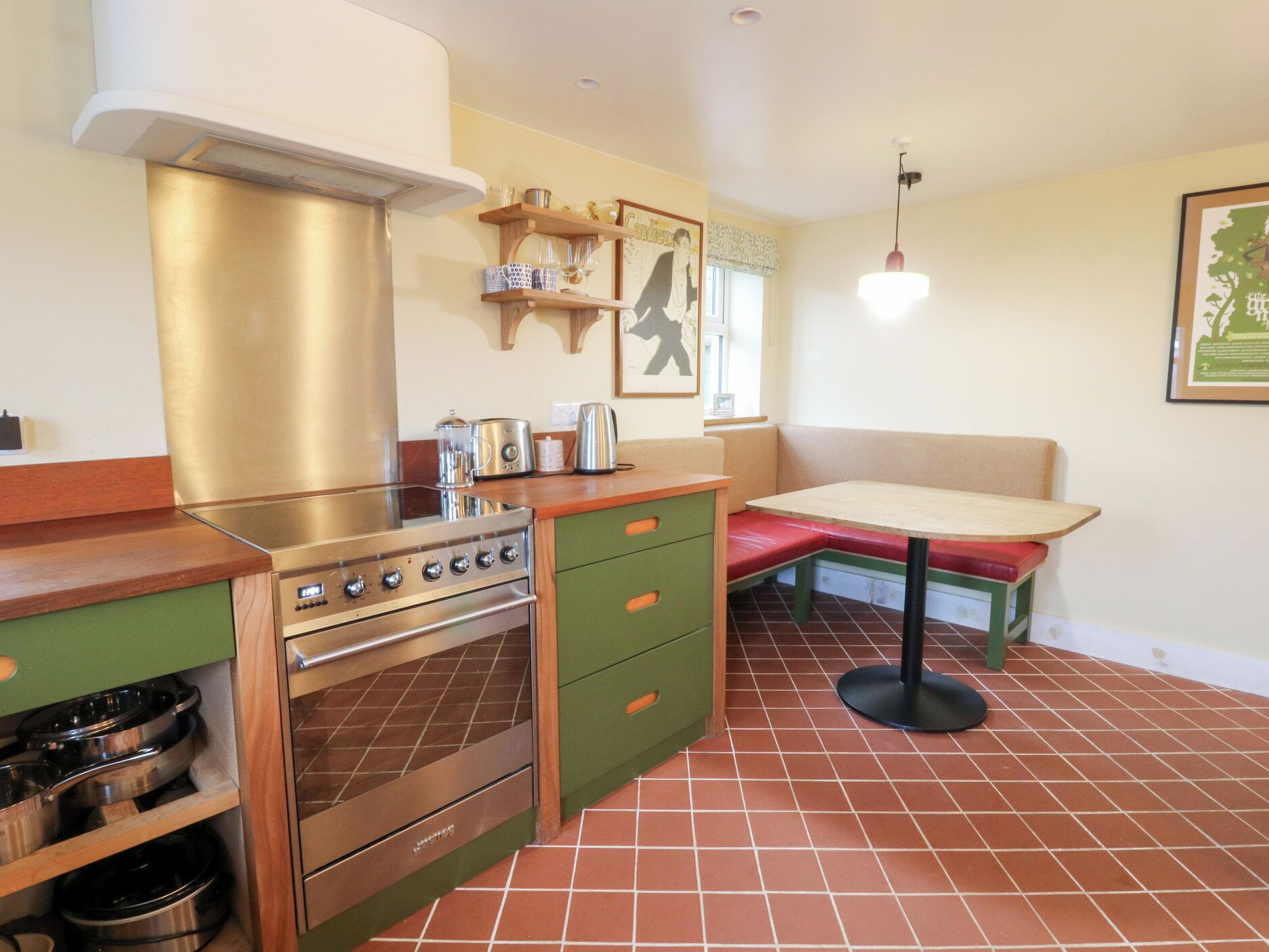 A compact kitchen with a stove, green cabinets, and a bench.