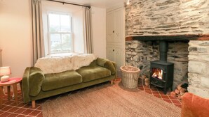 Una sala de estar acogedora con chimenea de piedra, un sofá verde y una ventana con cortinas.