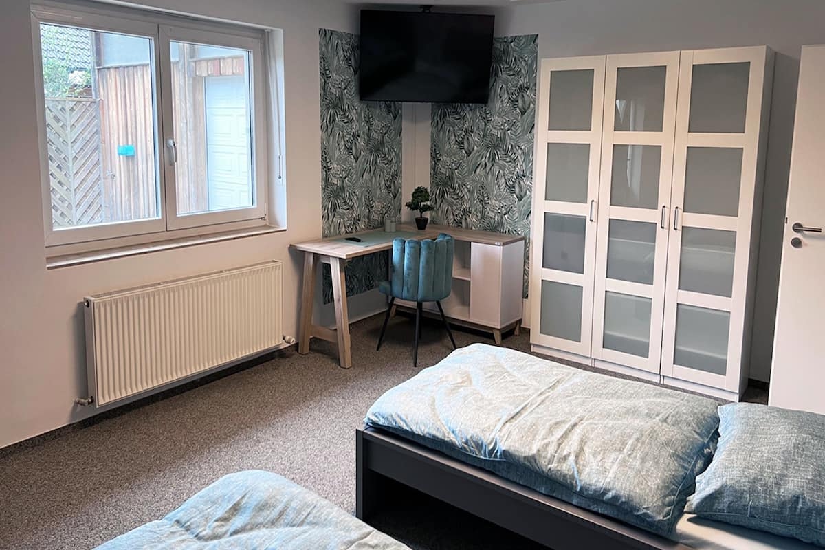 Een slaapkamer met twee bedden, een bureau, een stoel, een kledingkast en een televisie.