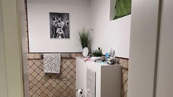 A compact bathroom with a white toilet, a small sink, and a mirror. There is a green towel hanging on the wall and a picture frame above the toilet.