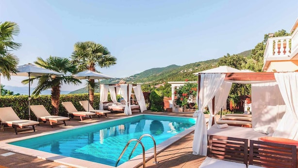 A pool area with lounge chairs, a canopy, and a view of the hills. - Villa Chiara Opatija Apartment Moderna (Ičići)
