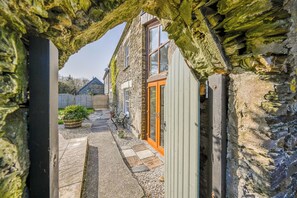 Un bâtiment en pierre avec une porte et des fenêtres en bois, un chemin et un banc.