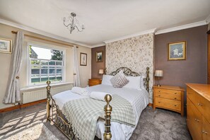 Une chambre à coucher avec un lit à baldaquin, une table de chevet en bois, une commode et une fenêtre avec des rideaux.