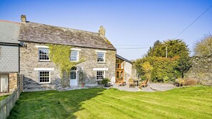 A stone house with a well-maintained lawn, a wooden door, and a patio area with outdoor furniture. - The Old Farmhouse (Looe)
