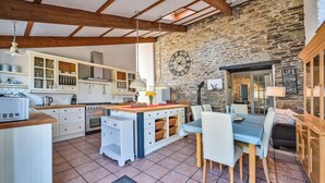 A spacious kitchen with white cabinetry, a stone wall, and a dining area with a table and chairs. - The Old Farmhouse (Looe)