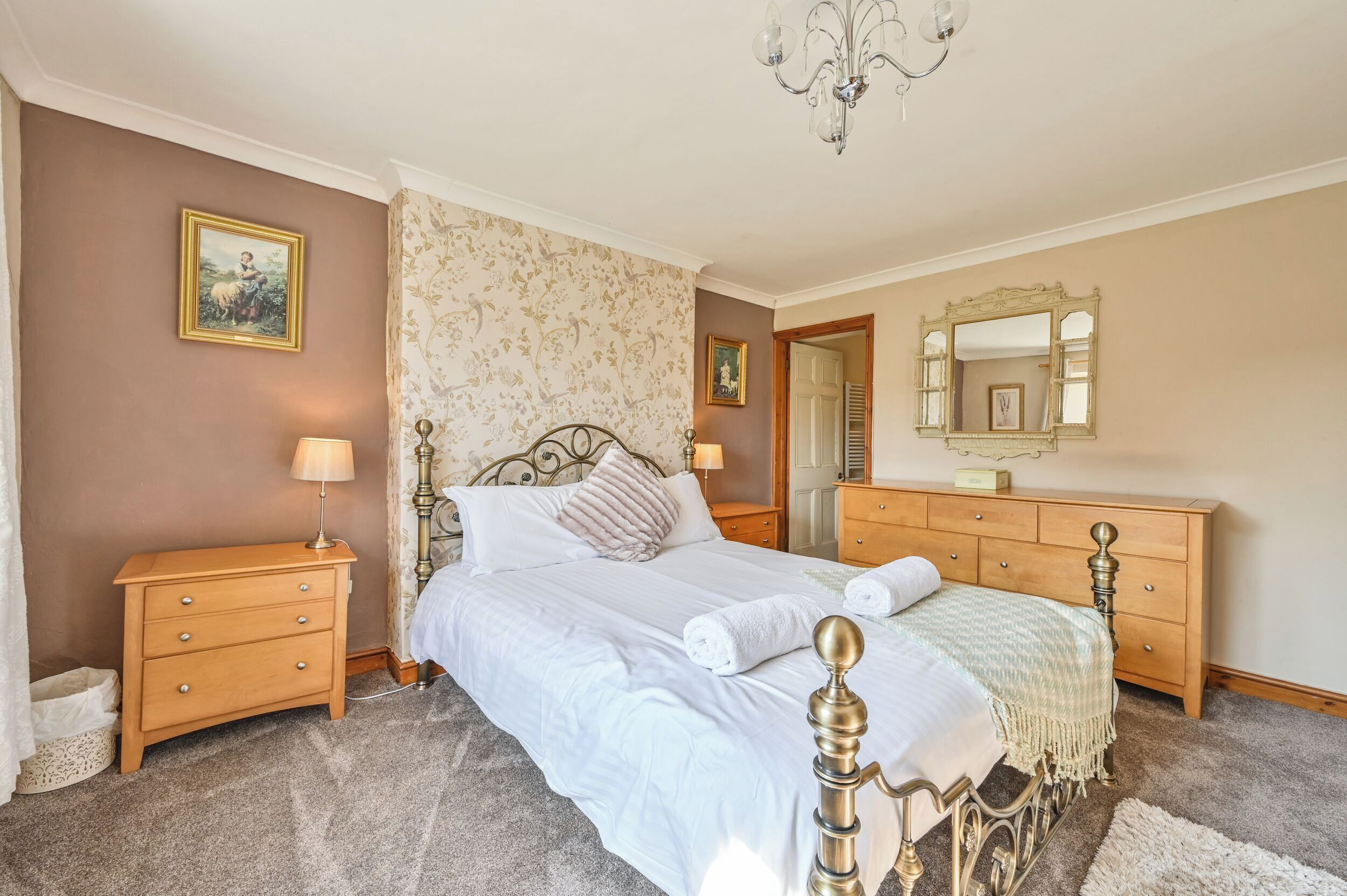 Een keurig opgemaakte slaapkamer met een bed, nachtkastjes, een dressoir en een spiegel.
