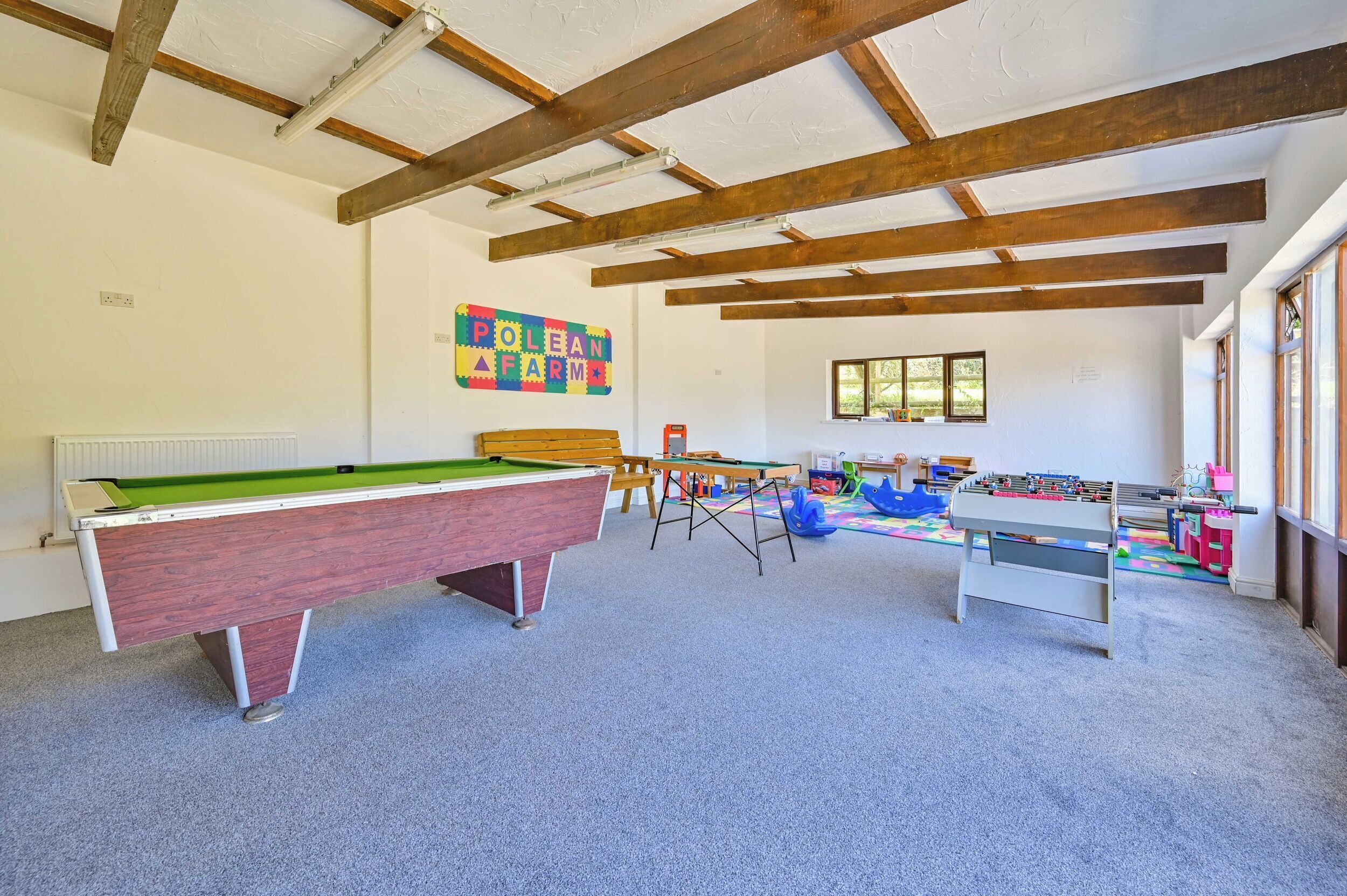 A room with a pool table, foosball table, and a colorful sign on the wall.