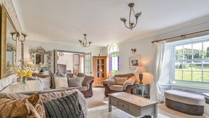 A spacious living room with a large sofa, a coffee table, and a view of a garden through a window. - The Old Farmhouse (Looe)