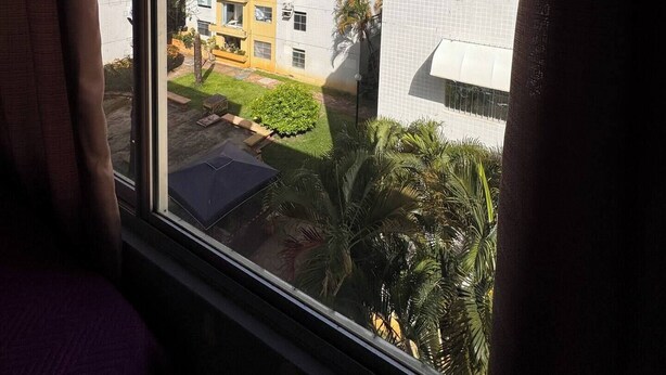 Vista dalla finestra di un complesso residenziale con diversi edifici, un piccolo giardino e un cielo blu limpido.