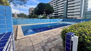 Una piscina con piastrelle in pietra, circondata da una recinzione blu, adiacente a un edificio moderno a più piani.