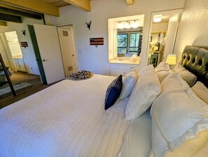 A bedroom with a large bed, a window with a view, a mirror, and a door. - Snow Summit Townhouse Unit #9 (Big Bear Lake)