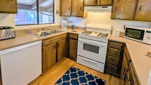 Una cucina con mobili in legno, una lavastoviglie bianca, un fornello, un lavandino e un forno a microonde.
