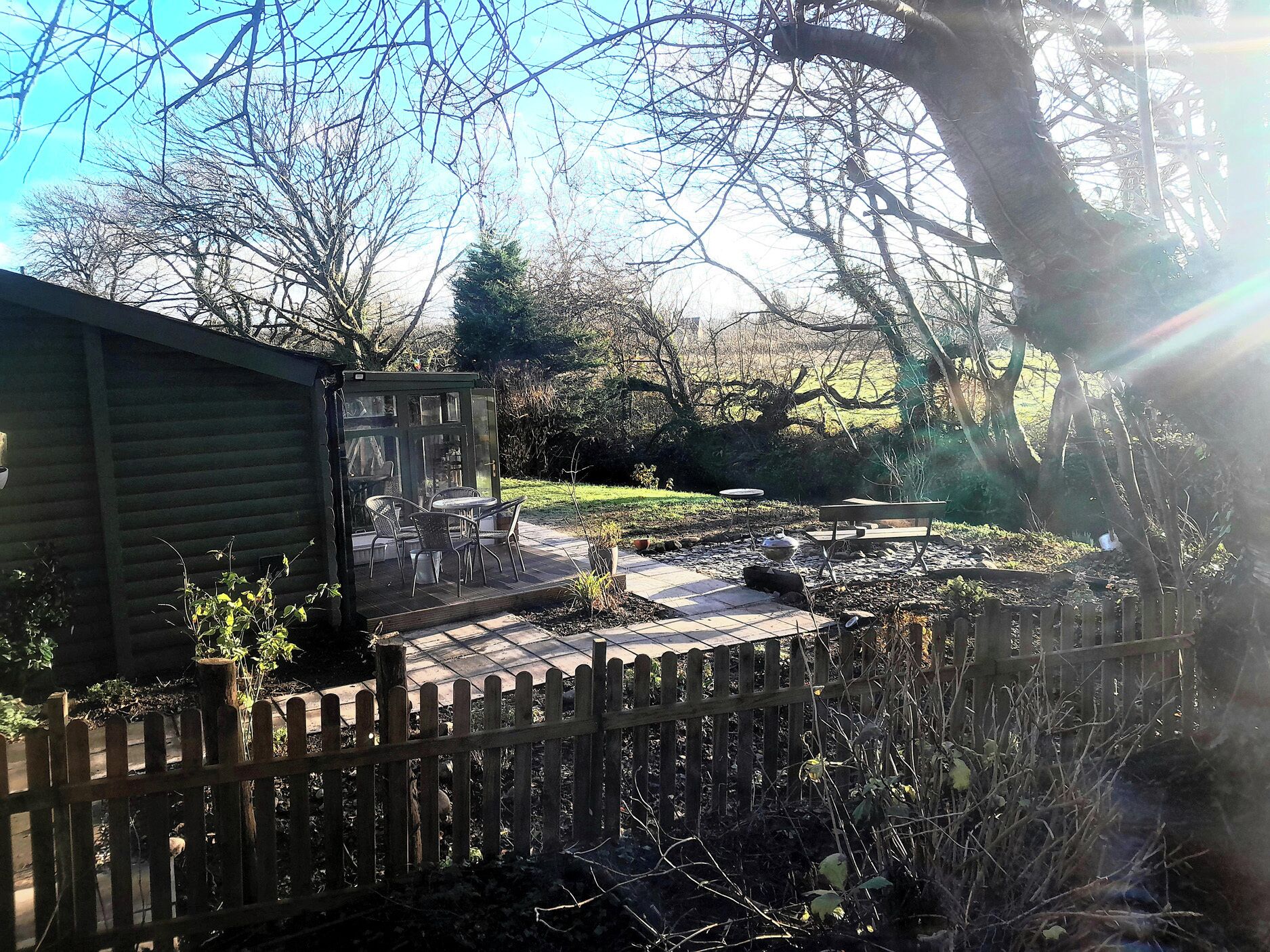 A patio with a table and chairs, a wooden fence, and a garden area with trees and shrubs.