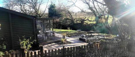 A patio with a table and chairs, a wooden fence, and a garden area with trees and shrubs.