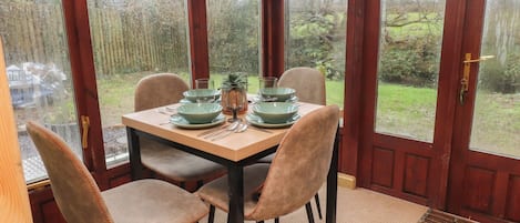 Een eetgedeelte met een houten tafel voor vier personen, omringd door stoelen met oranje stiksel.