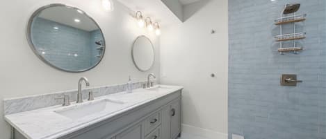 A modern bathroom with two sinks, a large mirror, and a shower with a glass enclosure.