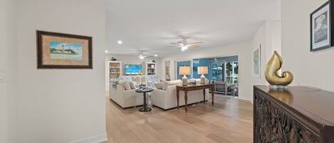 A spacious living room with a white sofa, a wooden coffee table, and a TV in the background.