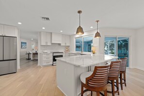 Une cuisine moderne avec des meubles blancs, un îlot central et un coin bar avec des chaises en bois.
