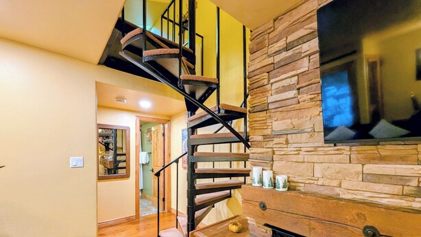 A staircase with a wooden finish and metal railings, leading to a second floor. A stone wall with a mounted television is visible on the right. - New Listing: Pool, Hot Tub, Free shuttle (Keystone)