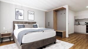 Quarto moderno com cama grande, roupeiro embutido e pequena cozinha compacta.