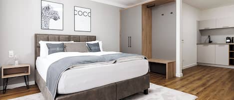 A modern bedroom with a large bed, a built-in wardrobe, and a small kitchenette.