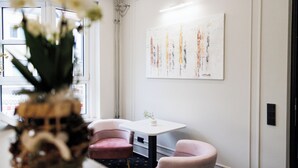 Quarto moderno com parede branca, um quadro, uma mesa pequena e duas cadeiras cor-de-rosa.