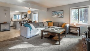 A modern living room with a grey sofa, a glass coffee table, and a kitchen in the background. - Freshly updated 1 bedroom in the heart of town close to everything! (Mammoth Lakes)