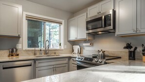 A modern kitchen with a large island, stainless steel appliances, and a window with a view of trees. - Freshly updated 1 bedroom in the heart of town close to everything! (Mammoth Lakes)