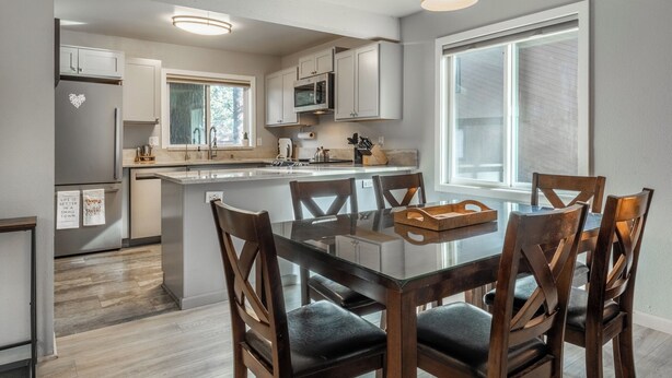 A modern kitchen with white cabinets, a central island, and a dining area with wooden chairs and a glass table. - Freshly updated 1 bedroom in the heart of town close to everything! (Mammoth Lakes)