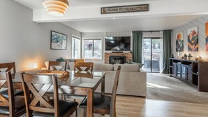 A spacious living room with a fireplace, a dining area with wooden chairs, and a large TV mounted on the wall. - Freshly updated 1 bedroom in the heart of town close to everything! (Mammoth Lakes)