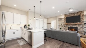 Une cuisine moderne avec des meubles blancs, un îlot central, des luminaires suspendus et une cheminée en pierre.