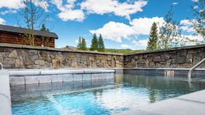 Un mur de pierre entoure une piscine, et on aperçoit un chalet en bois à l’arrière-plan.
