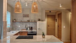 Eine moderne Küche mit einer zentralen Kochinsel, Pendelleuchten, einem Kühlschrank und einer Holztür.