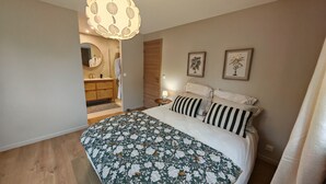 Ein Schlafzimmer mit floralem Bettbezug, einem Holzschrank, einem runden Spiegel und zwei gerahmten Bildern an der Wand.