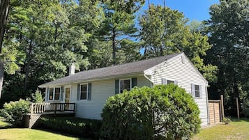 A single-story house with a front porch, surrounded by dense trees and a well-maintained lawn.