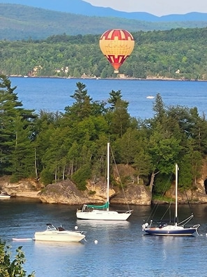 A coastal scene with a hot air balloon, boats, and a forested shoreline. - Spacious Beach Cabin w/ Lake Access 4BR (Colchester)
