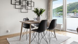 A modern dining area with a wooden table, black chairs, and a white rug. A potted plant and wine glasses are on the table.
