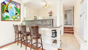 A kitchen with a granite countertop, a coffee maker, and a bar stool area. - Hale Ho‘omalie- Peaceful Mānoa Valley Retreat near UH (Honolulu)