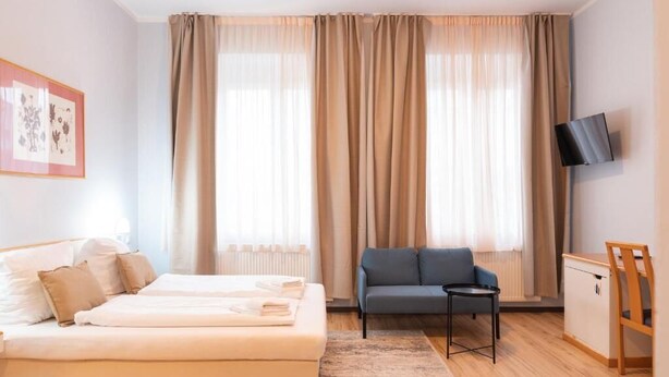 A hotel room with a bed, a sofa, a small table, a TV, and a desk. - UNEA Aparthotel Leipzig (Leipzig)